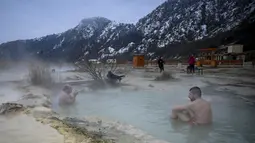 Orang-orang menikmati air panas di mata air mineral alami pada hari musim dingin di dekat desa Rupite, Bulgaria (2/2/2022). Penduduk setempat percaya bahwa air mineral menyembuhkan banyak penyakit dan gangguan. (AFP/Nikolay Doychinov)