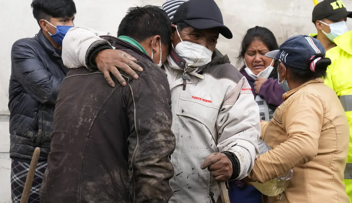 Warga saling menghibur saat jenazah ditemukan setelah banjir bandang yang memenuhi aliran sungai terdekat yang merusak mekanisme penahanan dan meruntuhkan lereng bukit membawa gelombang lumpur ke rumah-rumah di daerah La Gasca di Quito, Ekuador, Selasa (1/2/2022). (AP Photo/Dolores Ochoa)