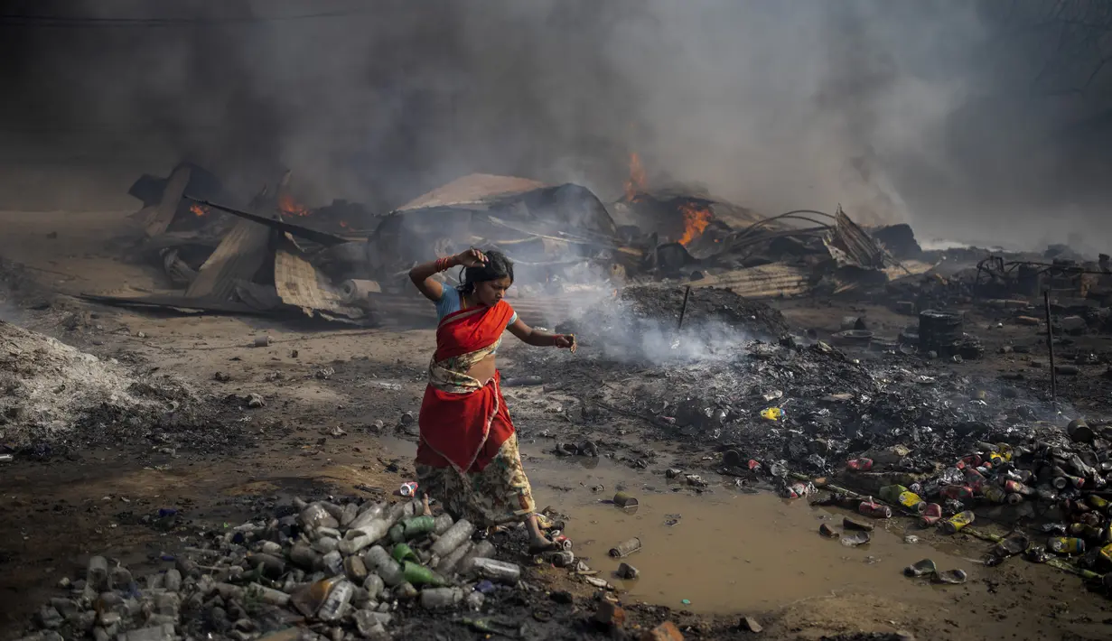 Seorang wanita berjalan tanpa alas kaki di dekat gubuk yang terbakar di daerah kumuh di Noida, pinggiran kota New Delhi, India, Minggu (11/4/2021). Dua anak tewas dan lebih dari 150 gubuk kumuh yang sebagian besar dihuni oleh para pemulung dalam kebakaran pada Minggu sore. (AP Photo/Altaf Qadri)