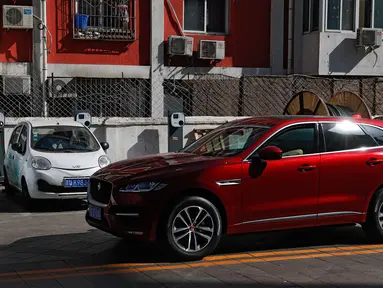 Sebuah mobil SUV warna merah melintas di depan mobil listrik model lama yang diparkir di stasiun pengisian listrik di rumah hunian Beijing (14/04/2017). Penjualan mobil kesulitan karena minimnya stasiun pengisian listrik. (AP Photo / Andy Wong)