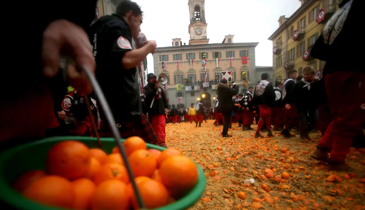 Peserta membawa jeruk saat perang-perangan selama karnaval di kota Ivrea, Italia, Minggu (7/2). Peserta yang dibagi menjadi dua tim ini saling melempar jeruk menggunakan kostum dan aksesoris lengkap. (REUTERS/Stefano Rellandini)