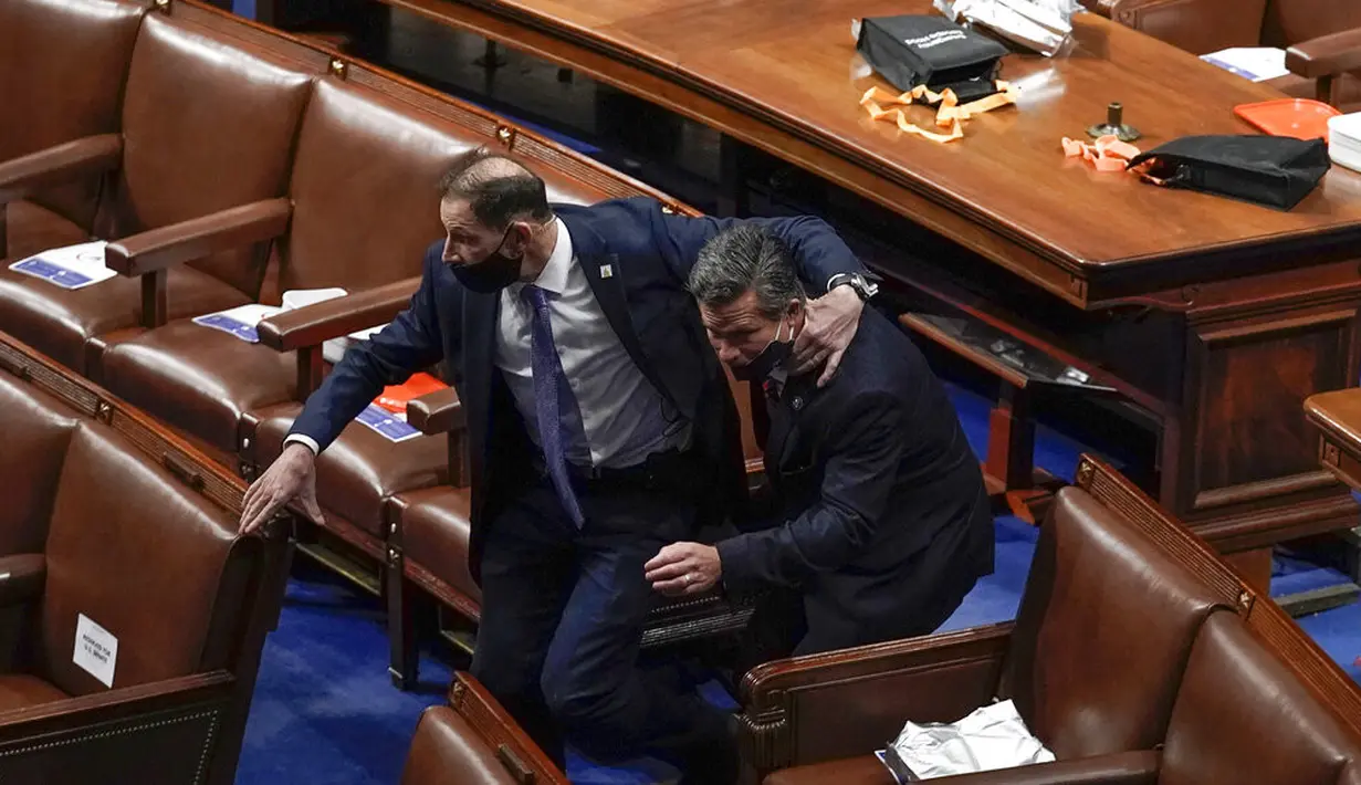 Anggota parlemen berlari mengevakuasi diri saat para pengunjuk rasa mencoba masuk ke Gedung Capitol Hill di Washington DC, Amerika Serikat, Rabu (6/1/2021). Gedung Capitol Hill berhasil diamankan oleh polisi dan sejumlah demonstran dikeluarkan dari area gedung. (AP Photo/J. Scott Applewhite)