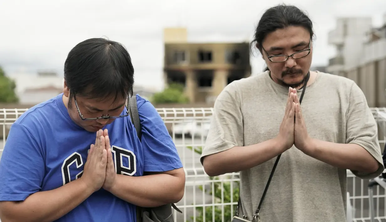 Dua pria berdoa untuk para korban kebakaran  di gedung Kyoto Animation Studio di Kyoto, Jepang (19/7/2019). Stasiun televisi NHK melapor, seorang pria yang menuangkan bensin ke sekitar gedung animasi telah ditahan. (AP Photo/Jae C. Hong)