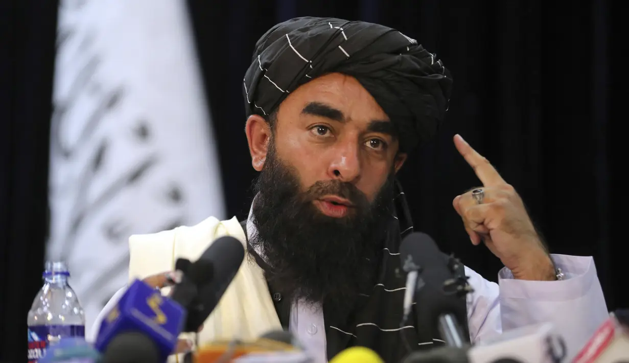 Di depan bendera Taliban, juru bicara Taliban Zabihullah Mujahid berbicara pada konferensi pers pertamanya, di Kabul, Afghanistan, pada Selasa (17/8/2021). Mujahid yang selama ini misterius, muncul pertama kalinya di hadapan wartawan pada Selasa waktu setempat. (AP Photo/Rahmat Gul)