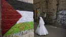 Seorang gadis Yahudi ultra-Ortodoks yang mengenakan kostum berjalan di samping dinding yang dicat dengan cat semprot dengan bendera Palestina selama perayaan hari libur Yahudi Purim di lingkungan ultra-Ortodoks Mea Shearim di Yerusalem (28/2/2021). (AP Photo/Oded Balilty)