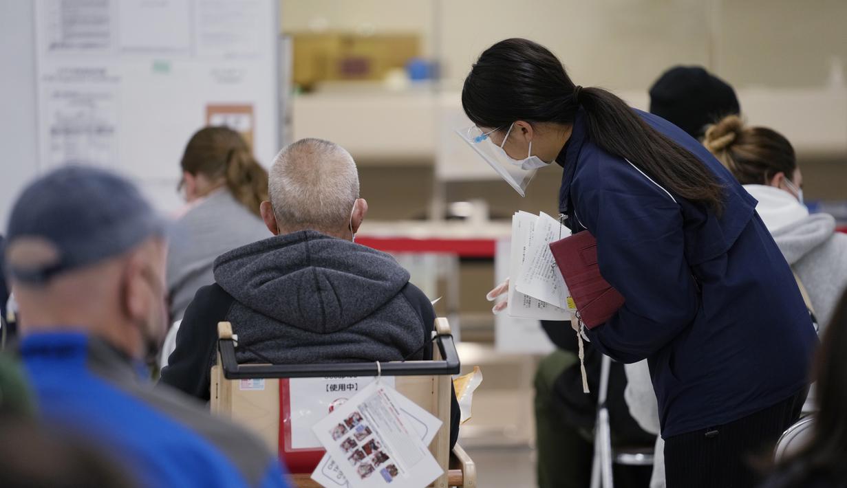 Seorang staf membantu penumpang menyiapkan dokumen mereka selama proses karantina pencegahan virus corona mereka setelah mendarat di Bandara Internasional Narita di Narita, timur Tokyo, Jepang (2/12/2021). (AP Photo/Hiro Komae)