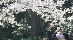 Orang-orang yang memakai masker mengambil foto bunga sakura di Tokyo, Selasa (23/3/2021). Keadaan darurat virus Covid-19 di Tokyo dan tiga provinsi sekitarnya resmi dicabut pada akhir hari Minggu, 21 Maret 2021. (AP Photo/Koji Sasahara)