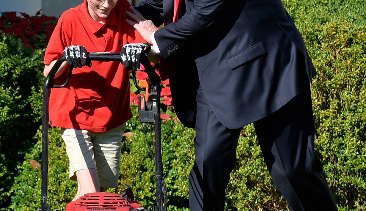 Presiden AS, Donald Trump membantu Frank Giaccio mendorong mesin pemotong rumput di Rose Garden, Gedung Putih, Jumat (15/9). Dalam suratnya, bocah 11 tahun itu menulis bahwa ini adalah kehormatan baginya memotong rumput Gedung Putih. (Mike Theiler/AFP)