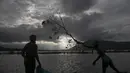 Seorang nelayan India melempar dahan pohon ke air untuk menarik ikan saat mereka meletakkan jala ikan mereka saat senja di surutnya air banjir di sawah di pinggiran Gauhati, India, Senin, (14/9/2020). (AP Photo / Anupam Nath)