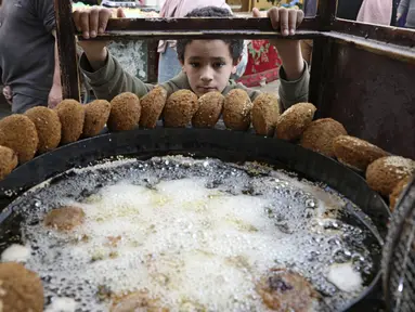 Seorang anak laki-laki Palestina menunggu sejumlah falafel di sebuah penjual di kota Hebron di Tepi Barat yang diduduki, selama bulan suci Ramadhan, Minggu (18/4/2021). Falafel adalah sebuah makanan Timur Tengah yang pada bulan Ramadhan, sering dimakan sebagai hidangan buka puasa. (HAZEM BADER/AFP)