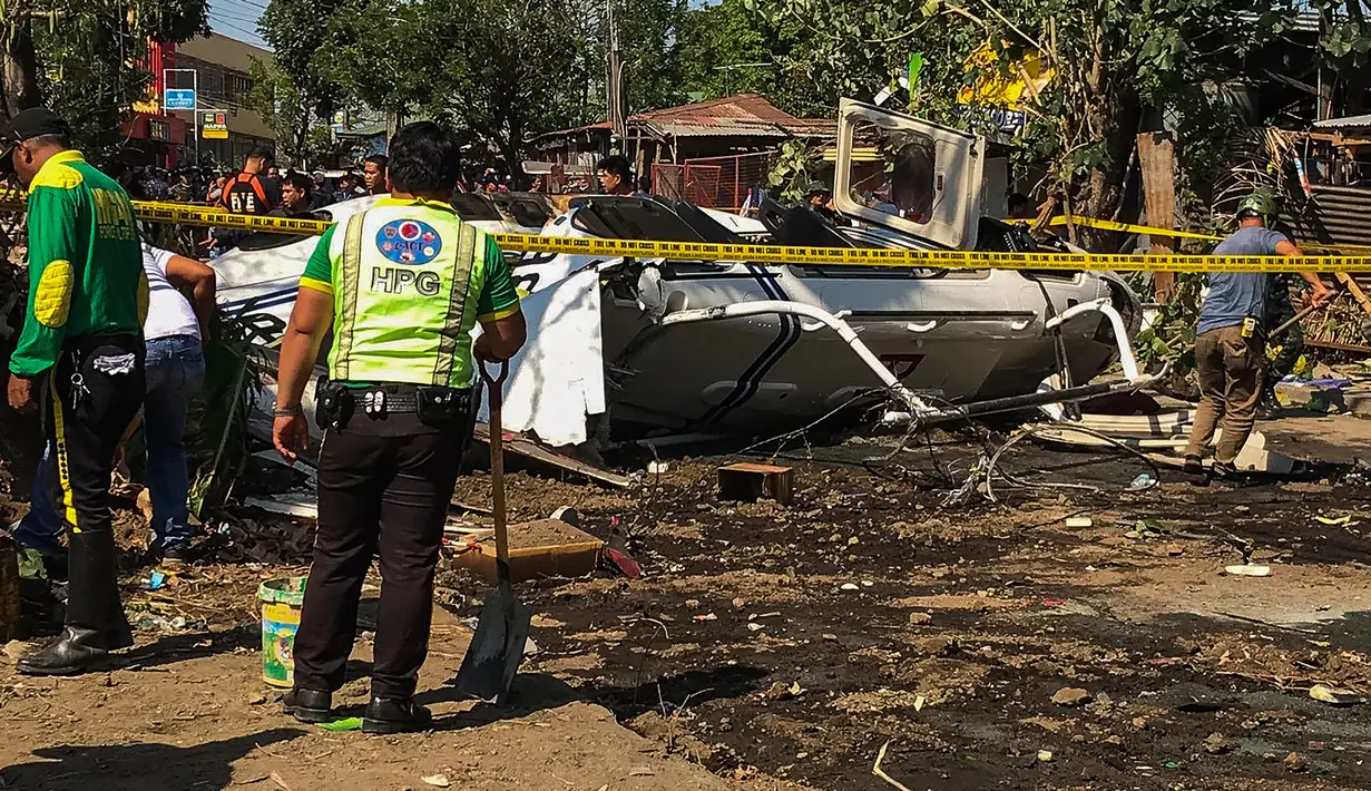 Penyelidik berdiri di dekat puing-puing Helikopter bell 429 yang membawa kepala polisi Filipina setelah jatuh di Kota San Pedro, selatan Manila, Kamis (5/3/2020). Saat helikopter lepas landas, debu beterbangan dan menciptakan awan debu tebal hingga mempengaruhi visibilitas di daerah tersebut.  (AFP)
