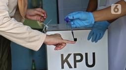 Petugas menandai jari warga dengan tinta usai mencoblos saat Pilkada Depok di TPS 56, Mekarjaya, Depok, Rabu (9/12/2020). TPS 56 menggunakan tema kesehatan untuk menarik warga menggunakan hak pilih dan mengingatkan protokol kesehatan di masa Pandemi COVID-19.  (Liputan6.com/Herman Zakharia)