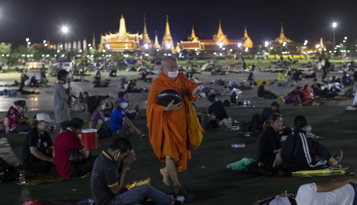 Seorang biksu Buddha berjalan membagikan masker wajah kepada pengunjuk rasa pro-demokrasi yang menduduki Sanam Luang, sebuah lapangan bersejarah untuk unjuk rasa semalam saat fajar di Bangkok, Thailand (20/9/2020). (AP Photo / Gemunu Amarasinghe)