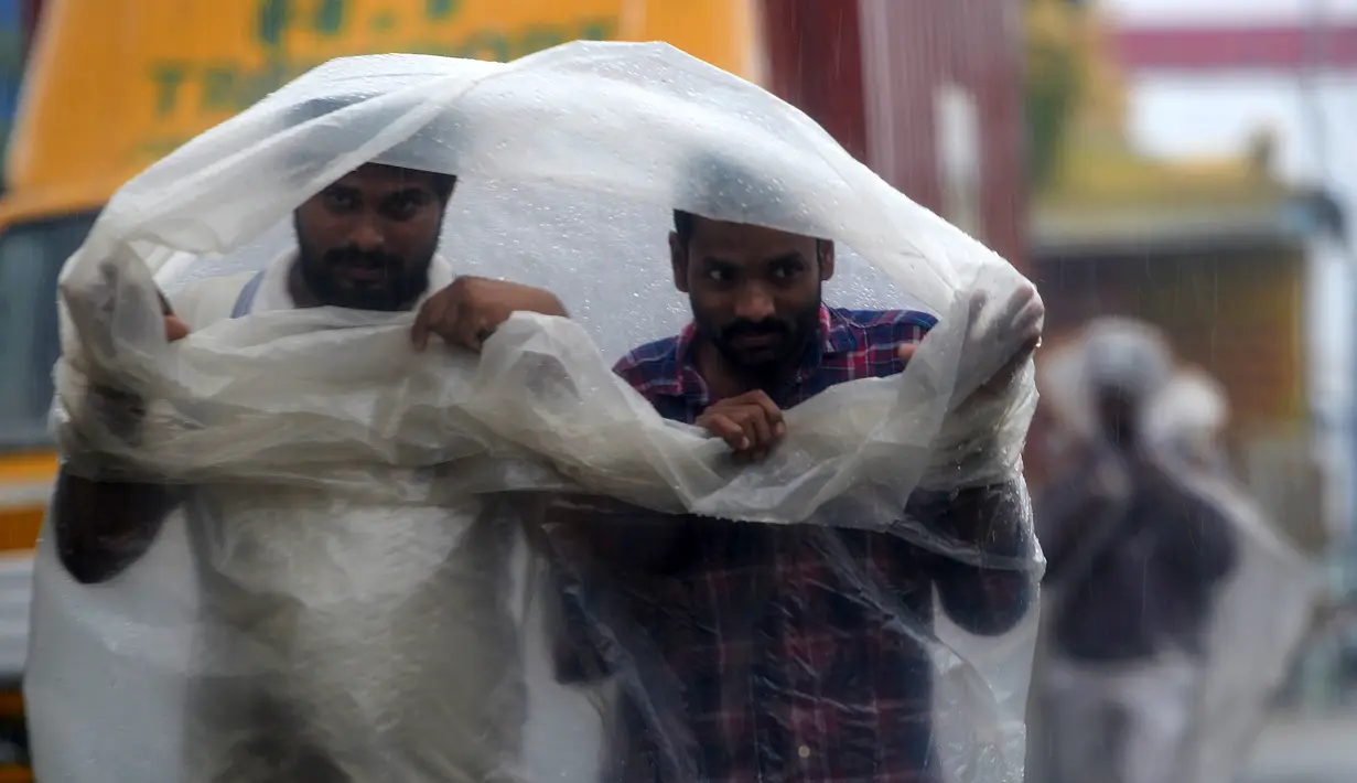 Dua pria menggunakan lembaran plastik untuk menutupi hujan lebat di Chennai saat topan Nivar mendekati pantai tenggara negara itu (25/11/2020). (AFP/Arun Sankar)