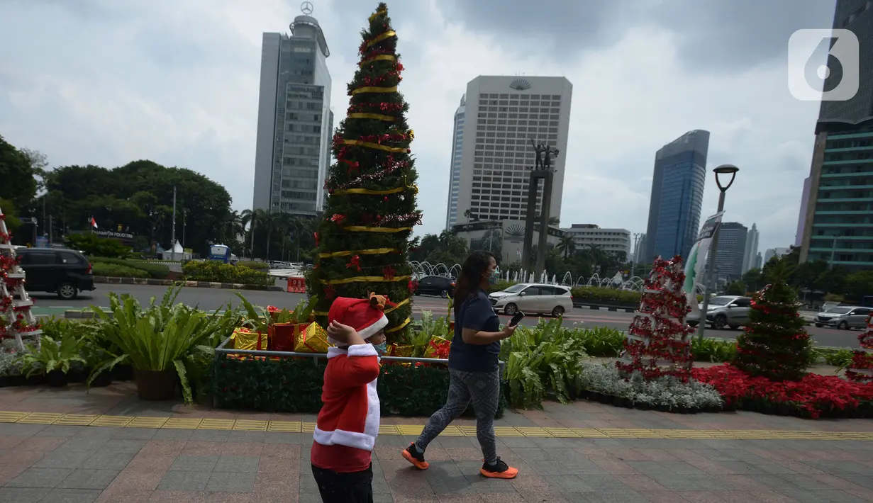 Warga DKI Jakarta melintas di dekat hiasan pohon Natal 2021 di Bundaran HI, Jakarta, Sabtu (25/12/2021). Libur Natal 2021 dimanfaatkan sebagian warga berfoto berlatar pohon Natal yang telah dihias atau berjalan-jalan ke mal untuk mengisi waktu berlibur bersama. (merdeka.com/Imam Buhori)
