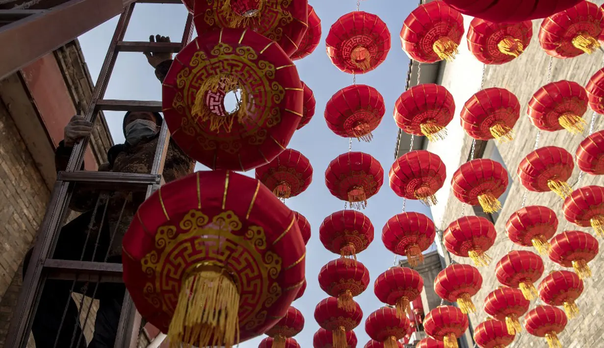 Seorang pekerja memasang lentera tradisional Tiongkok di sepanjang gang menjelang Tahun Baru Imlek di Beijing, China, 2 Februari 2021. Imlek tahun ini jatuh pada tanggal 12 Februari 2021. (NOEL CELIS/AFP)