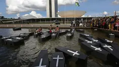 Sejumlah orang menceburkan replika peti mati saat menggelar aksi protes di luar gedung Kongres Nasional di Brasilia, Brasil (25/4). Mereka menuntut pertanggung jawaban atas terbunuhnya orang Indian karena masalah demarkasi lahan. (AP Photo/Eraldo Peres)