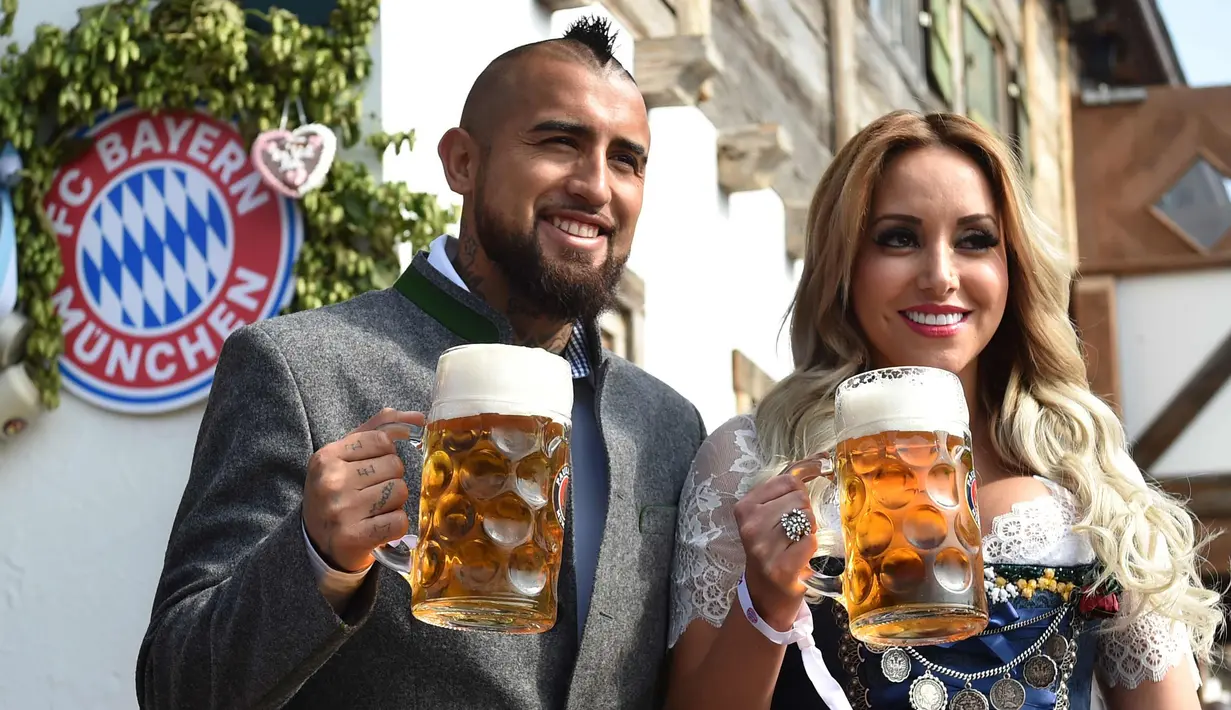Gelandang Bayern Munchen, Arturo Vidal dan istrinya, Maria Teresa Matus memegang cangkir bir saat mereka berpose selama festival bir Oktoberfest 2017 di Munich, Jerman (23/9). (AFP Photo/Christof Stache)