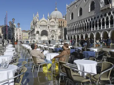 Orang-orang duduk di bar di St. Mark's Square yang terendam banjir di Venesia, Italia, Jumat (5/11/2021). Setelah Venesia mengalami banjir terparah kedua dalam sejarahnya pada November 2019, kota itu dibanjiri empat kali pasang luar biasa dalam waktu enam minggu. (AP Photo/Luigi Costantini)