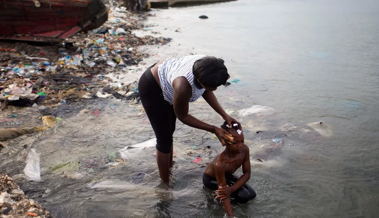 Seorang wanita memandikan putrinya di pantai saat mereka bersiap-siap untuk pergi ke gereja, di Warf of Port Cite Soleil di Port-au-Prince, Haiti (17/3). Cité Soleil merupakan lingkungan yang sangat miskin dan padat penduduk. (AP Photo/Dieu Nalio Chery)