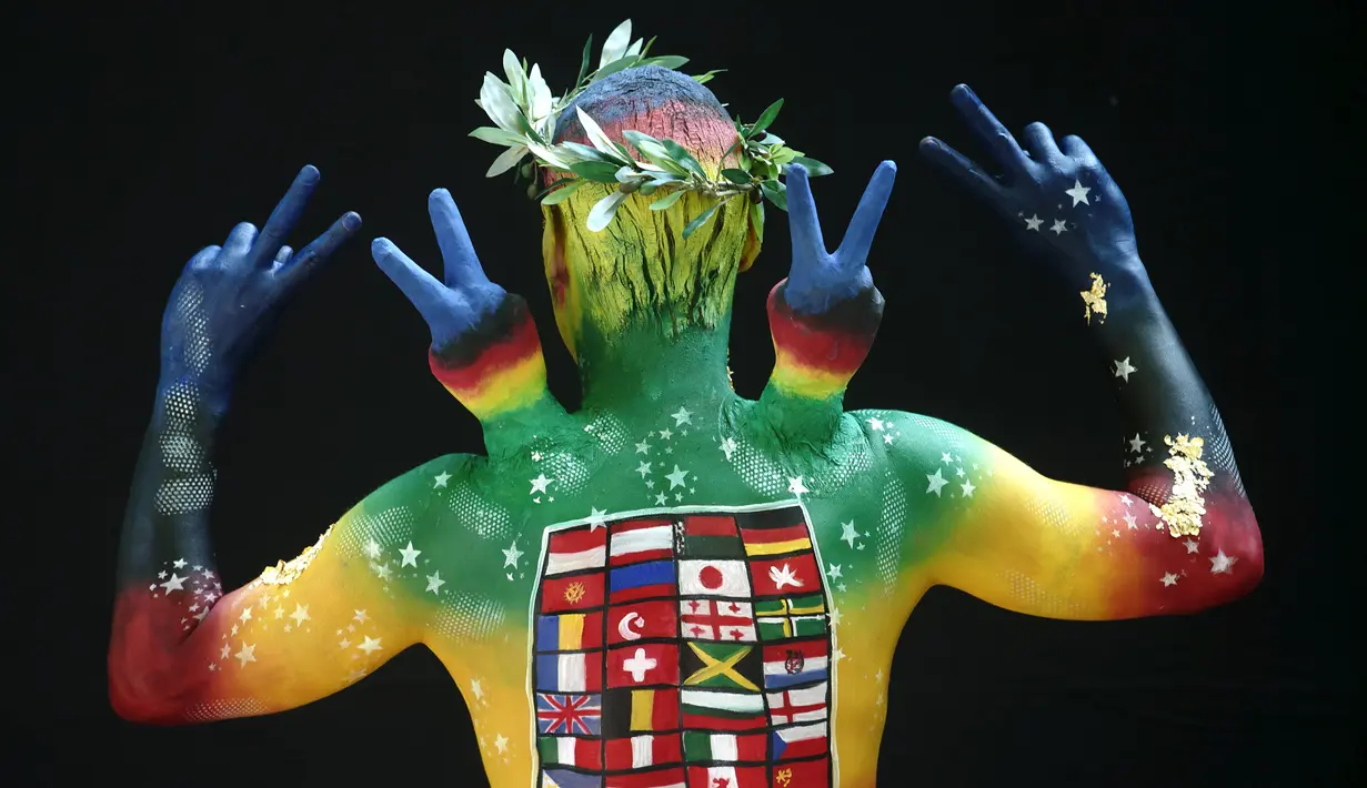 Model berpose menghadap ke belakang menunjukkan lukisan bendera negara-negara di dunia dan mengacungkan dua jari sebagai simbol perdamaian saat mengikuti Festival Bodypainting Dunia 2015 di Poertschach, Austria, (3/7/2015). (Reuters/Heinz-Peter Bade)