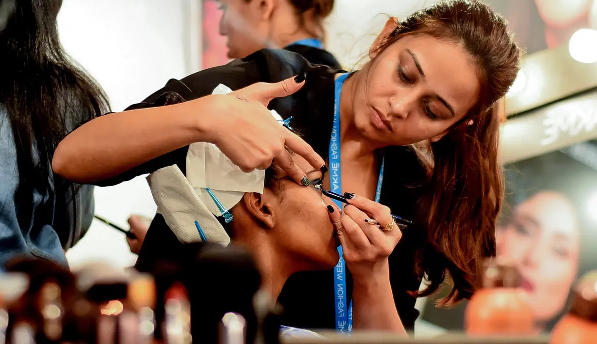 Seorang model India saat dirias oleh kru makeup di belakang panggung sebelum tampil di catwalk selama Lakmé Fashion Week (LFW) Summer Resort 2019 di Mumbai, India (31/1). (AFP Photo/Sujit Jaiswal)