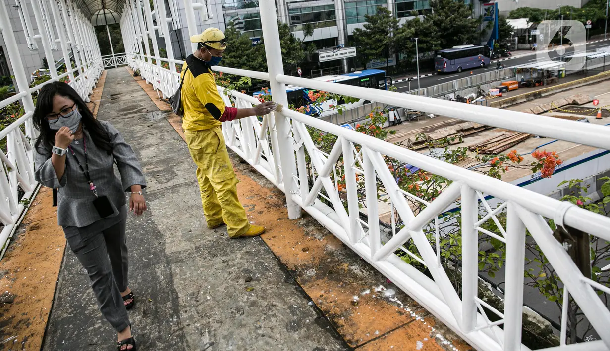 Warga melintasi pekerja Dinas Bina Marga DKI yang mengecat ulang tiang Jembatan Penyeberangan Orang (JPO) di kawasan Thamrin, Jakarta, Kamis (28/1/2021). Pengecatan ulang itu sebagai bagian dari perawatan JPO di Jakarta guna memberikan kesan bersih dan indah. (Liputan6.com/Faizal Fanani)