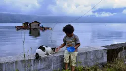 Seorang anak memberi makan seekor kucing di sebelah danau Laut Tawar di Takengon, provinsi Aceh tengah, (1/3). Suku Gayo menyebut danau ini dengan sebutan Danau Lut Tawar. (AFP Photo/Chaideer Mahyuddin)