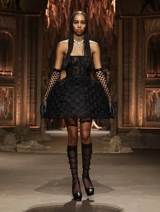 Model-model berjalan di landasan pacu dalam balutan rok melingkar lebar berbentuk lonceng, celana pendek renda, dan mantel hitam panjang yang dilapisi bunga bersulam. (Dok/DIOR).