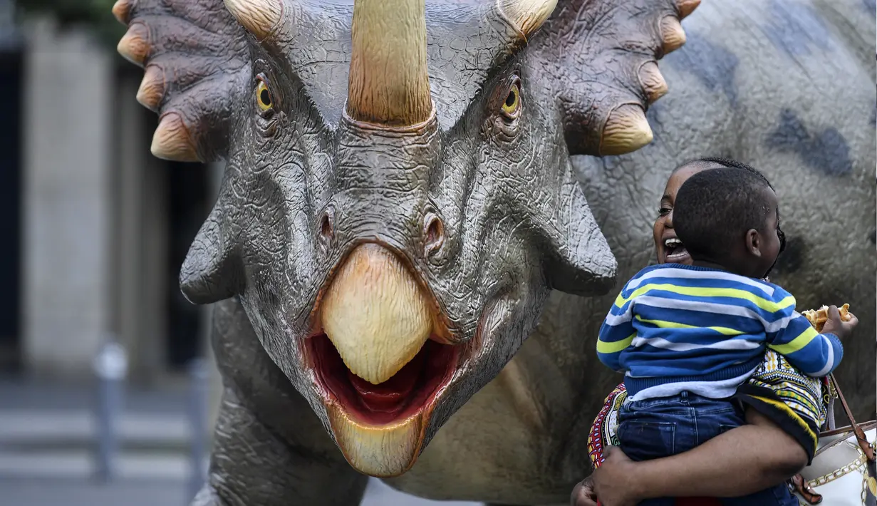 Seorang wanita mengendong anaknya berjalan di samping replika dinosaurus Styracosaurus seukuran aslinya di pusat kota Bochum, Jerman (12/8/2019). Pameran ini menampilkan 33 replika dinosaurus di sekitar pusat kota, berada di Bochum. (AP Photo/Martin Meissner)