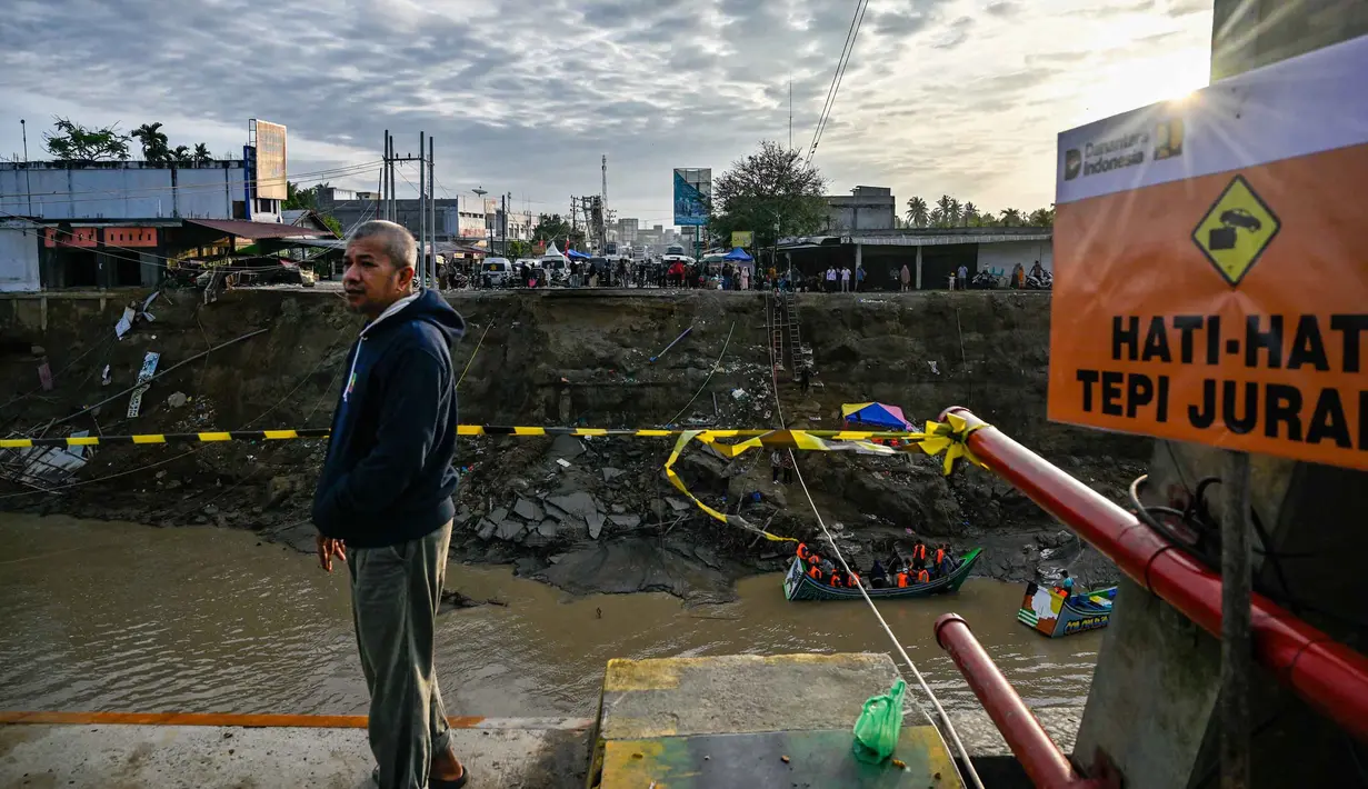 Salah satu sisi jembatan Kuta Blang runtuh akibat banjir bandang yang menerjang wilayah tersebut pada Kamis 27 November 2025 sore hari. Tampak dalam foto, seorang pria menyaksikan dari jembatan yang runtuh di atas Sungai Peusangan di Kuta Blang, Kabupaten Bireuen, Provinsi Aceh, Selasa 9 Desember 2025. (CHAIDEER MAHYUDDIN/AFP)
