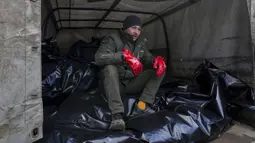 Seorang pekerja kamar jenazah duduk di atas kantong jenazah sebelum diangkut untuk dimakamkan di kuburan massal di pinggiran Mariupol, Ukraina, 9 Maret 2022. (AP Photo/Evgeniy Maloletka)