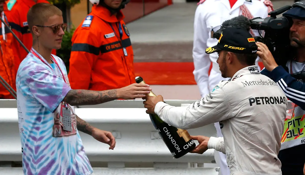 Pembalap Mercedes F1 Lewis Hamilton memberikan sampanye kepada penyanyi Justin Bieber usai berhasil menjuarai Grand Prix di Monaco, (29/5). Hamilton menjadi yang tercepat dengan mencatatkan waktu satu jam 59 menit 29,133 detik. (REUTERS/Eric Gaillard)