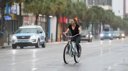 Seorang wanita muda mengendarai sepeda di tengah hujan di Ocean Boulevard di Pantai Myrtle, Carolina Selatan (3/8/2020). Badai Isaias terus bergerak ke utara di sepanjang pesisir timur AS. (Sean Rayford/Getty Images/AFP)