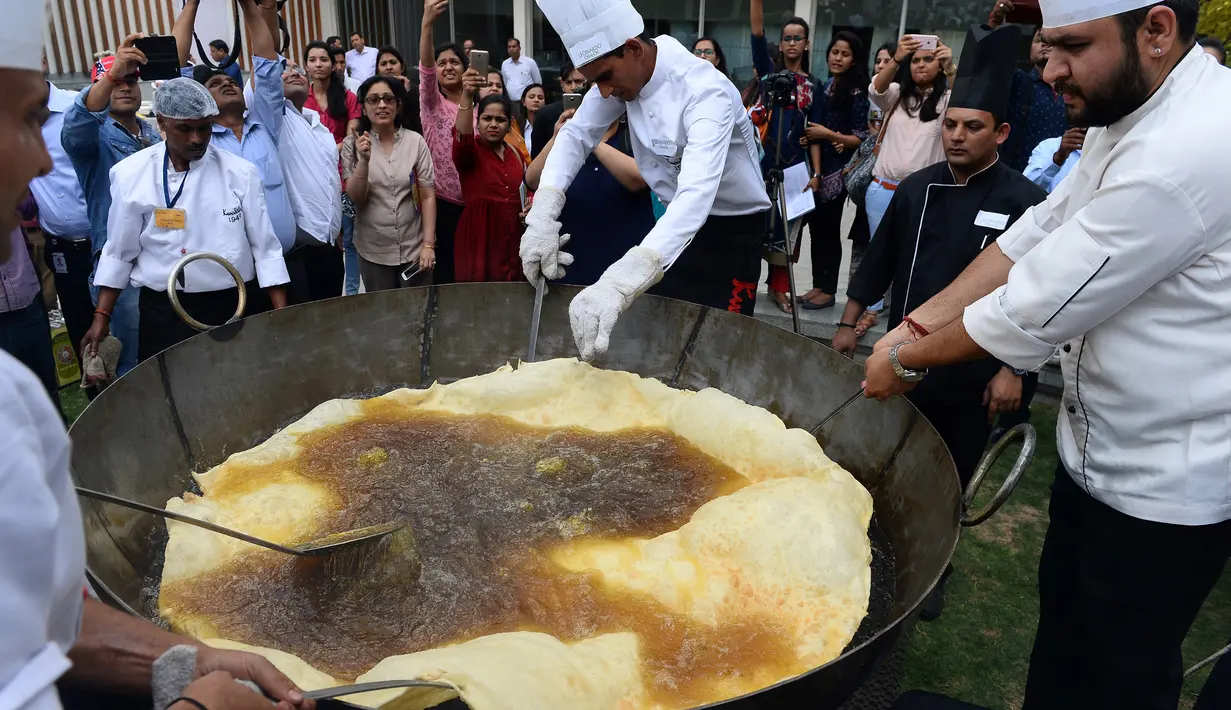 Proses penggorengan Bhatura dengan ukuran tak biasa di India, New Delhi, Kamis (6/4). Penyelenggara berharap Bhatura buatan mereka bisa memecahkan rekor Bhatura  terbesar di India. (AFP PHOTO / SAJJAD HUSSAIN)