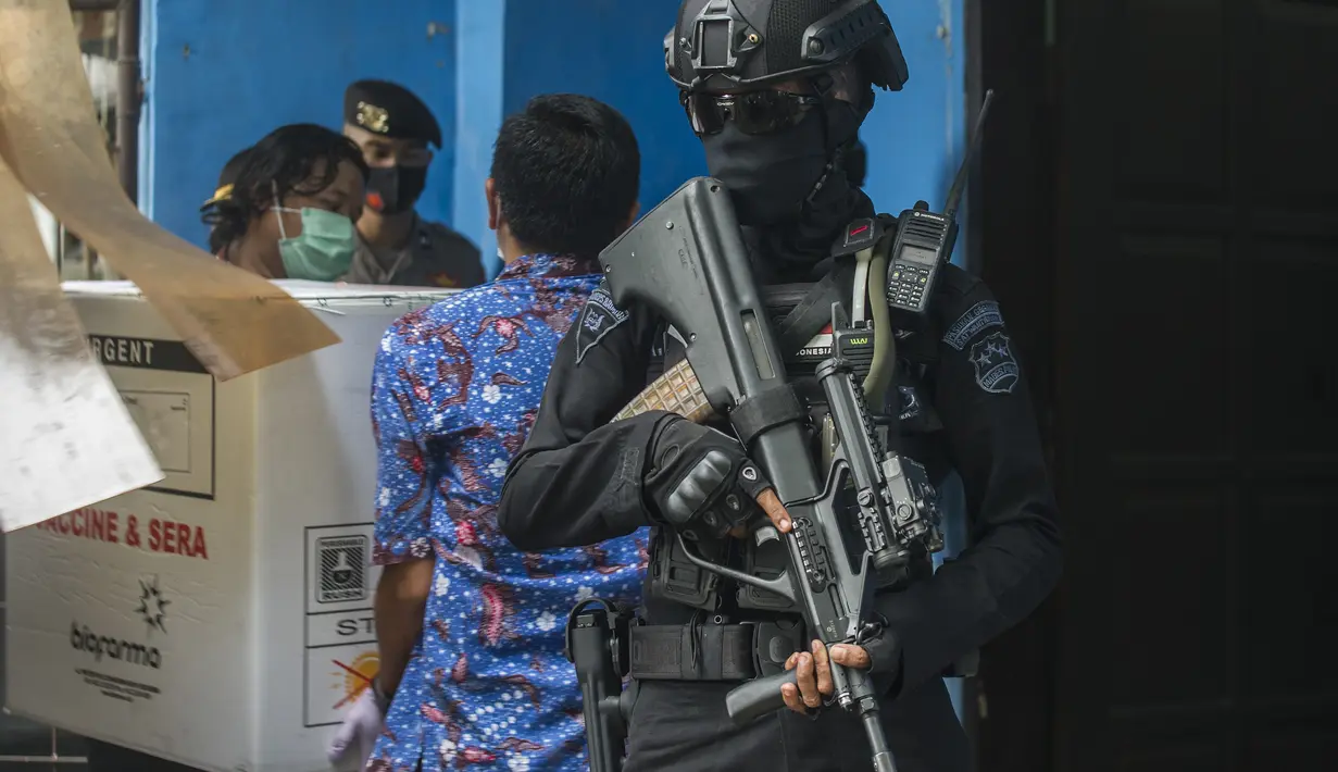 Polisi bersenjata bersiaga saat pekerja menurunkan vaksin COVID-19 produksi Sinovac dari truk setibanya di Surabaya pada Senin (4/1/2021).  Pemerintah mulai mendistribusikan 3 juta dosis vaksin Covid-19 asal perusahaan China, Sinovac, ke 34 provinsi Indonesia. (Photo by Juni Kriswanto / AFP)