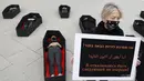 Seorang wanita memegang plakat bertulis "Saya menolak menjadi yang berikutnya" saat lainnya berbaring dalam peti mati tiruan mewakili yang tewas akibat kekerasan dalam rumah tangga jelang Hari Perempuan Internasional di luar Pengadilan Distrik, Tel Aviv, Israel, Minggu (7/3/2021). (JACK GUEZ/AFP)