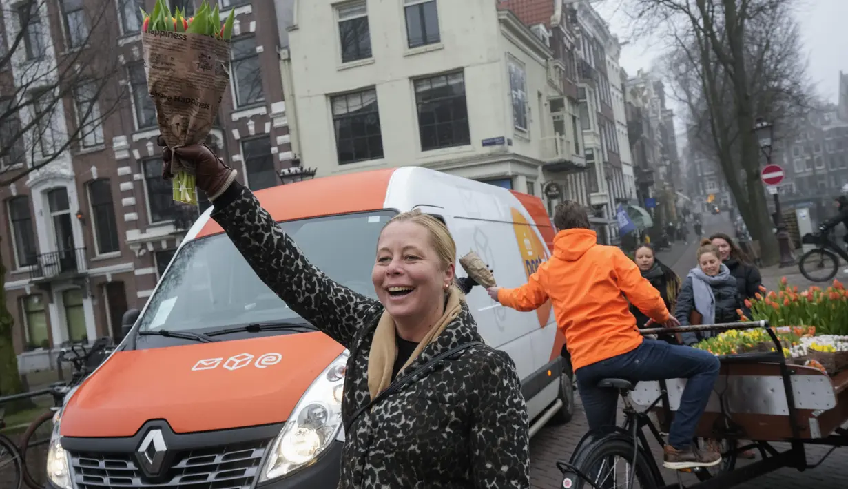 Warga mendapatkan buket tulip di Amsterdam, Belanda, Sabtu (15/1/2022). Suasana ibu kota Belanda semakin diringankan oleh garis-garis warna dalam bentuk dari ribuan tandan tulip gratis yang dibagikan para petani yang berlayar dengan perahu melalui kanal. (AP Photo/Peter Dejong)