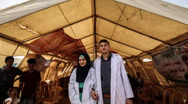 Pasangan petugas medis Muadh Al-Raqab (kanan) dan Hadeel Al-Najjar yang baru menikah berfoto di luar tenda di jalur Gaza selatan, Palestina (2/5). Petugas medis ini harus melangsungkan pernikahannya di dalam tenda. (AFP Photo/Said Khatib)