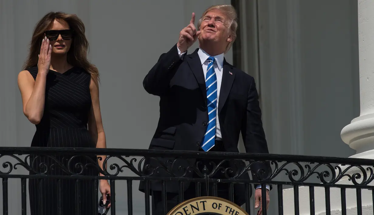 Presiden AS Donald Trump ditemani Ibu Negara, Melania Trump menunjuk ke atas saat menyaksikan  gerhana matahari dari balkon Gedung Putih di Washington, Senin (21/8). Trump tampak menatap langsung ke arah matahari dengan mata telanjang. (NICHOLAS KAMM/AFP)