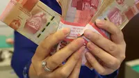 Petugas menunjukkan uang kertas rupiah di Bank BUMN, Jakarta, Selasa (17/4). Mengacu data Bloomberg, rupiah siang ini pukul 12.00 WIB di pasar spot exchange sebesar Rp 13.775 per dolar AS atau menguat 4,7 poin. (Liputan6.com/Angga Yuniar)