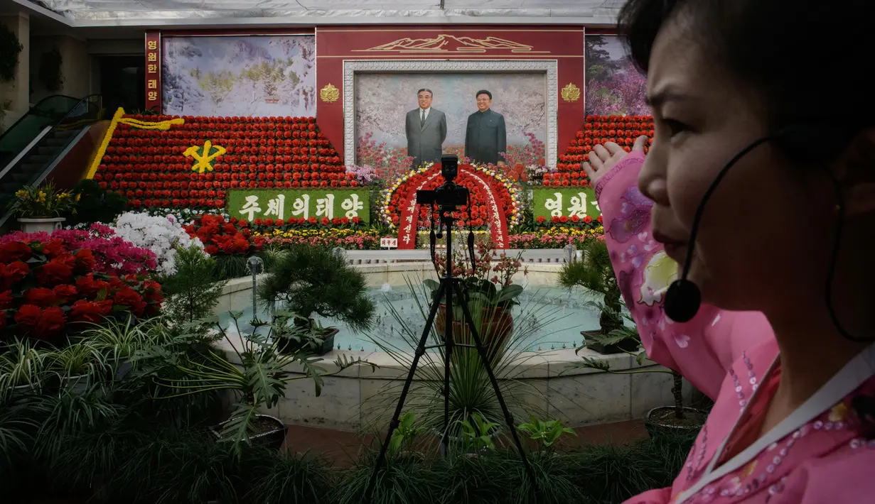 Pemandu memberi isyarat di depan potret pemimpin Korea Utara, Kim Il Sung dan Kim Jong Il pada pameran bunga 'Kimjongilia' di Pyongyang, Kamis (14/2). Korea Utara menggelar festival bunga merayakan ulang tahun mendiang ayah Kim Jong-un. (Ed JONES/AFP)