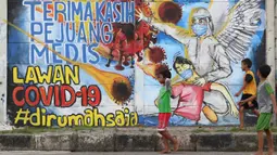 Anak anak melintasi mural ajakan melawan COVID-19 di Depok, Jawa Barat, Selasa (14/4/2020). Pemprov Jawa Barat akan memulai pembatasan sosial skala besar di Bogor, Depok, Bekasi pada Rabu (15/4) dengan menyiapkan anggaran Rp4 triliun sebagai jaring pengaman sosial. (Liputan6.com/Helmi Fithriansyah)