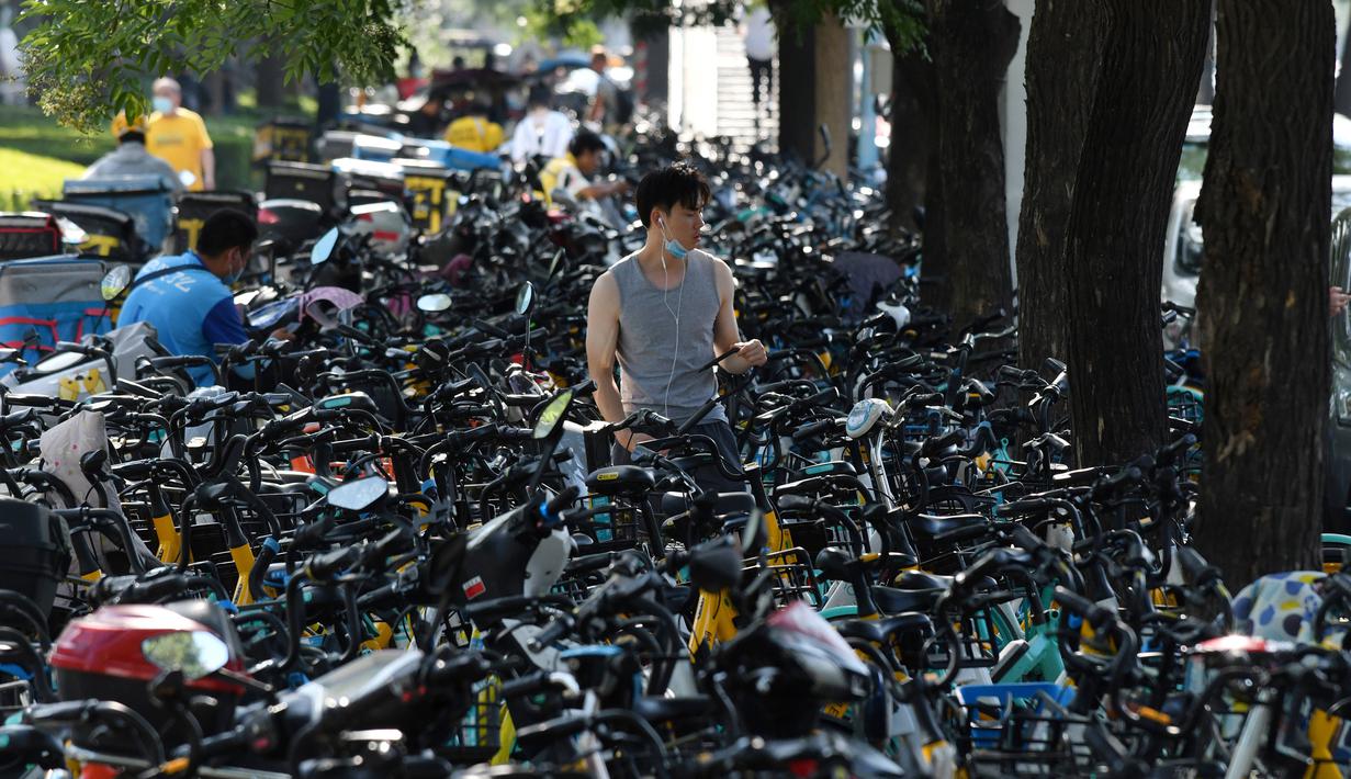 Seorang pria berjalan melintasi sepeda-sepeda yang diparkir memenuhi trotoar di Beijing, China (21/7/2020). Selama dua tahun terakhir, Pemerintah Beijing telah menyediakan fasilitas persewaan sepeda menggunakan sistem bike sharing. (AFP Photo/Greg Baker)
