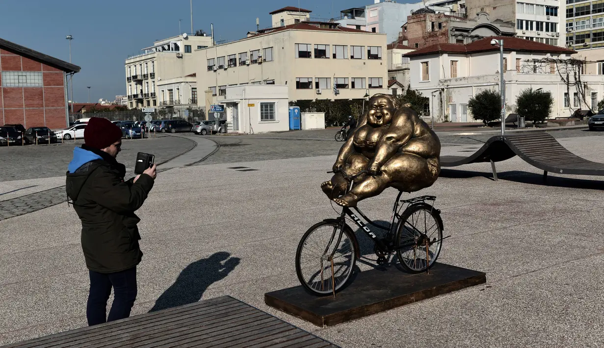 Seorang pria mengambil gambar patung karya seniman China Xu Hongfei di Thessaloniki, Yunani, Rabu (19/12). Sebanyak 15 patung karya Xu Hongfei menghiasi tepi pantai Thessaloniki. (Sakis Mitrolidis/AFP)