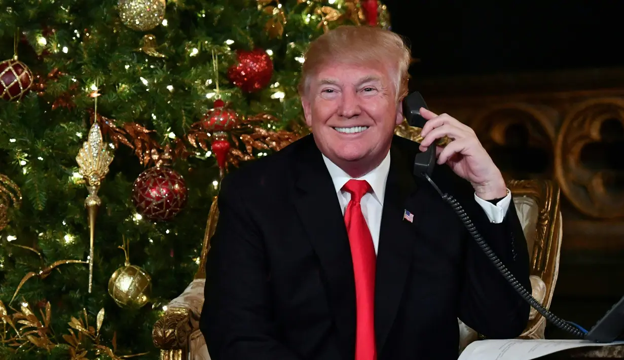 Presiden AS Donald Trump tersenyum saat berbicara di telepon pada malam natal di Palm Beach, AS (24/12). Donald Trump dan istrinya sibuk berbicara di telepon dengan anak-anak saat mengiktui NORAD Tracks Santa. (AFP Photo/Nicholas Kamm)