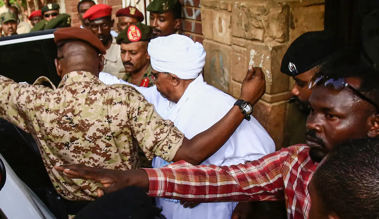 Mantan Presiden Sudan, Omar al-Bashir, dikawal setelah menghadap jaksa untuk pembacaan dakwaan terkait kasus korupsi di ibu kota Khartoum, Minggu (16/6/2019). Ini merupakan penampilan pertamanya di hadapan publik sejak kudeta penggulingan dirinya pada April lalu. (Yasuyoshi CHIBA/AFP)