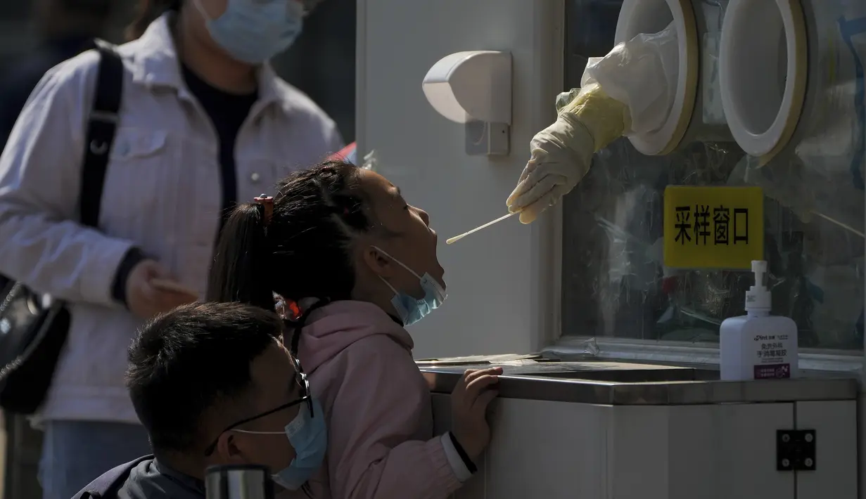 Seorang pria yang memakai masker membantu seorang anak untuk mendapatkan swab tenggorokan COVID-19 rutinnya di tempat pengujian virus corona di Beijing, Kamis (6/10/2022). Xinjiang yang luas adalah wilayah China terbaru yang terkena pembatasan perjalanan COVID-19, karena China semakin meningkatkan langkah-langkah pengendalian menjelang kongres penting Partai Komunis akhir bulan ini. (AP Photo/Andy Wong)