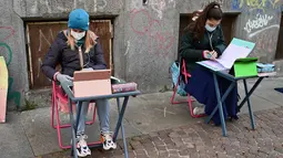 Anita Iacovelli (kiri) dan temannya Lisa Rogliatti, berusia 12 tahun, duduk di depan sekolah Italo Calvino di Turin, Italia, 17 November 2020. Anita memprotes penutupan sekolahnya karena pembatasan COVID-19 dengan duduk di luar gedung sambil mengikuti pelajaran jarak jauh. (Miguel MEDINA/AFP)
