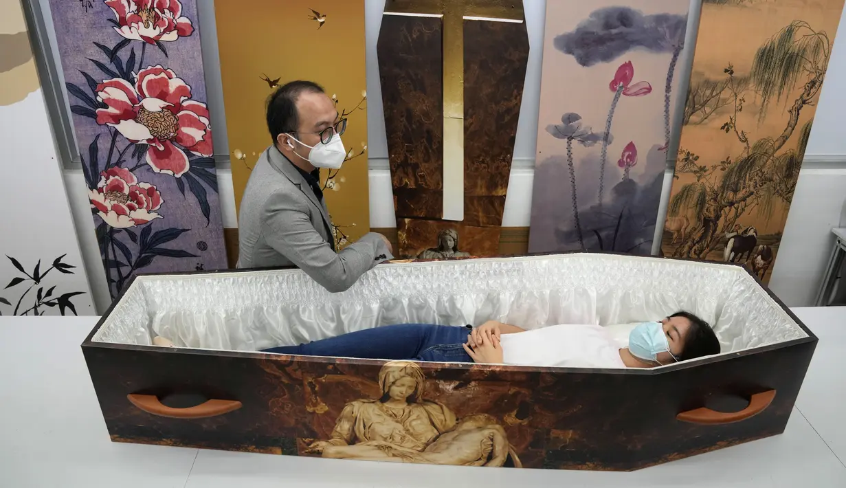 Wilson Tong, CEO LifeArt Asia berbicara dengan reporter yang mencoba peti mati kertas berdesain katolik di Hong Kong, Jumat, 18 Maret 2022. Hong Kong kekurangan peti mati selama wabah paling mematikan dari pandemi, yang telah menelan sekitar 6.000 nyawa sepanjang tahun ini. (AP Photo/Kin Cheung)